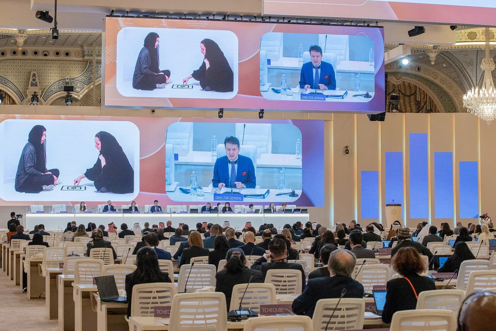قاعة مؤتمر في الرياض بشاشتين عملاقتين تنقلان المتحدثين وحضور على المقاعد